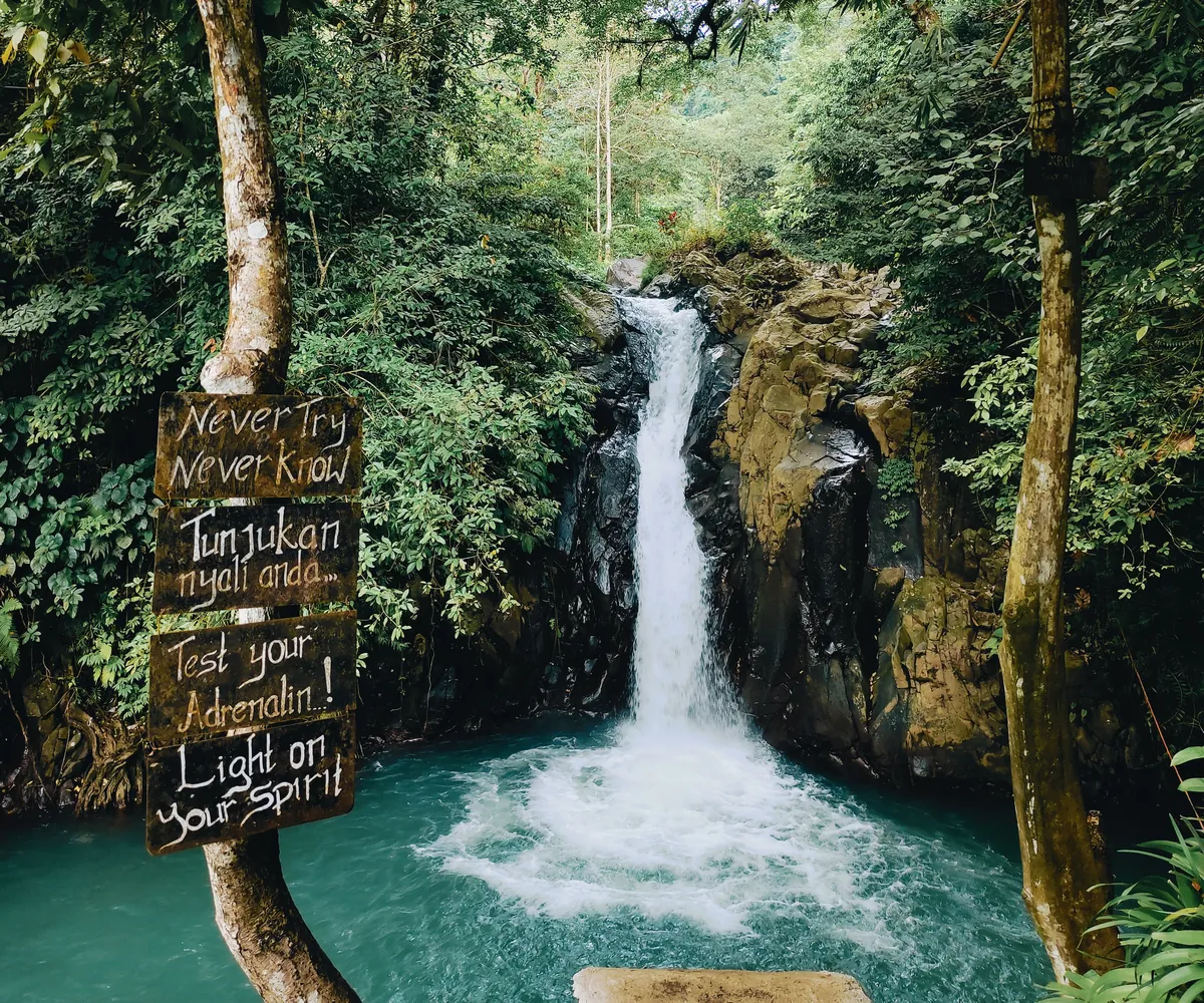Aling-Aling waterfall dropping into a turquoise pool, with a hand-painted sign beside it
