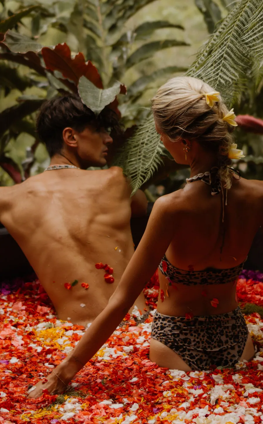 Couple seen from behind in a flower petal bath among tropical foliage