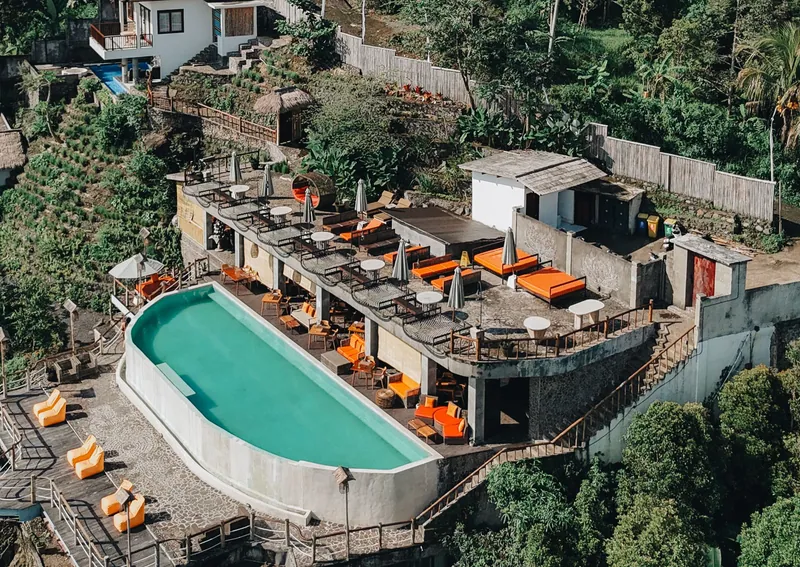 Aerial view of the resort pool and terraced buildings on a forested hillside
