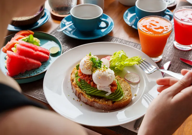 Breakfast table with avocado toast and a poached egg, sliced watermelon, juices and coffee